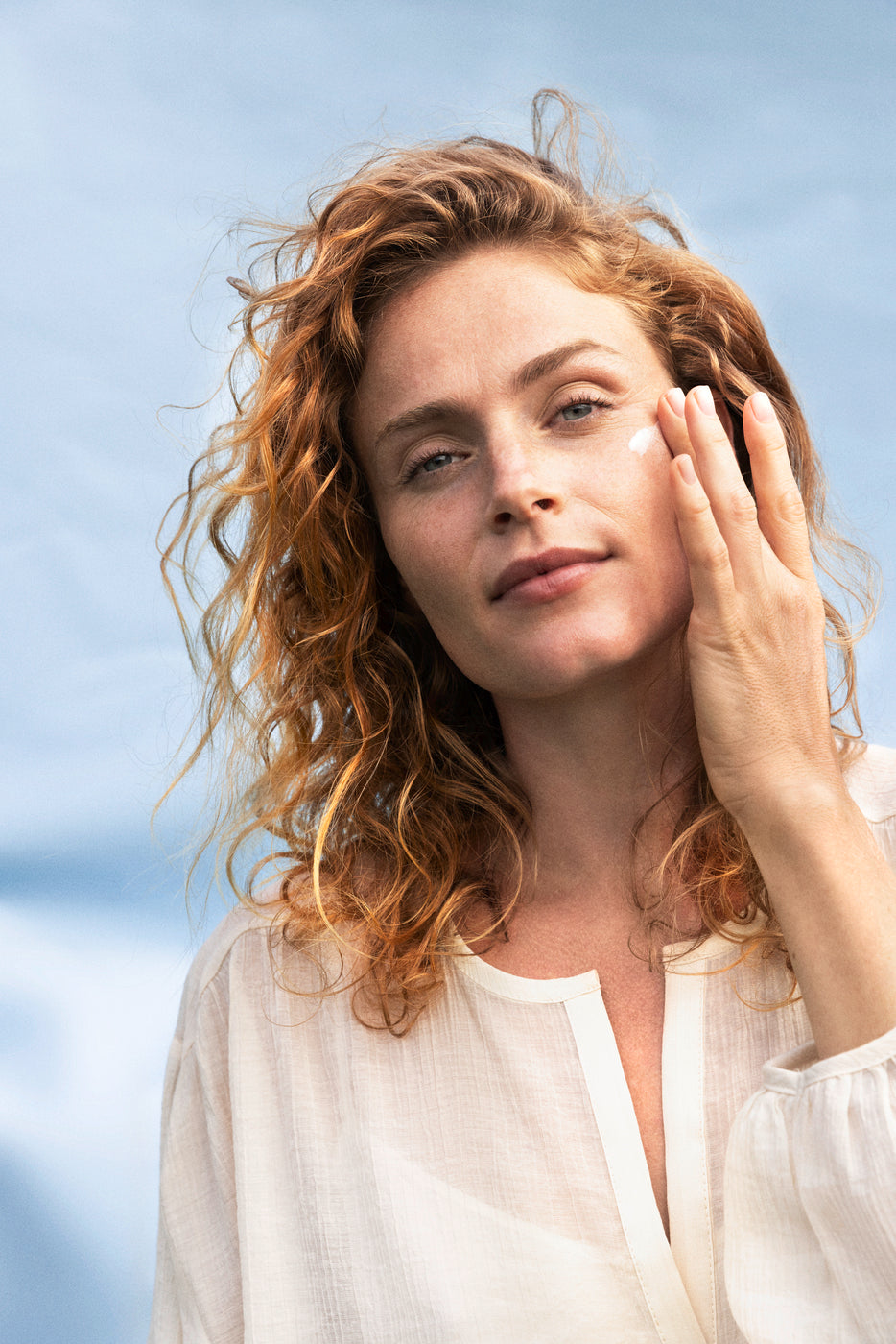 Donna con capelli ricci all'aperto si applica crema sul viso