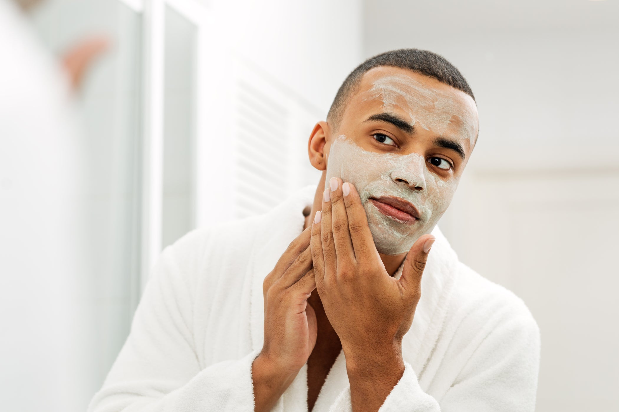 Giovane uomo con carnagione scura applica una maschera viso in bagno