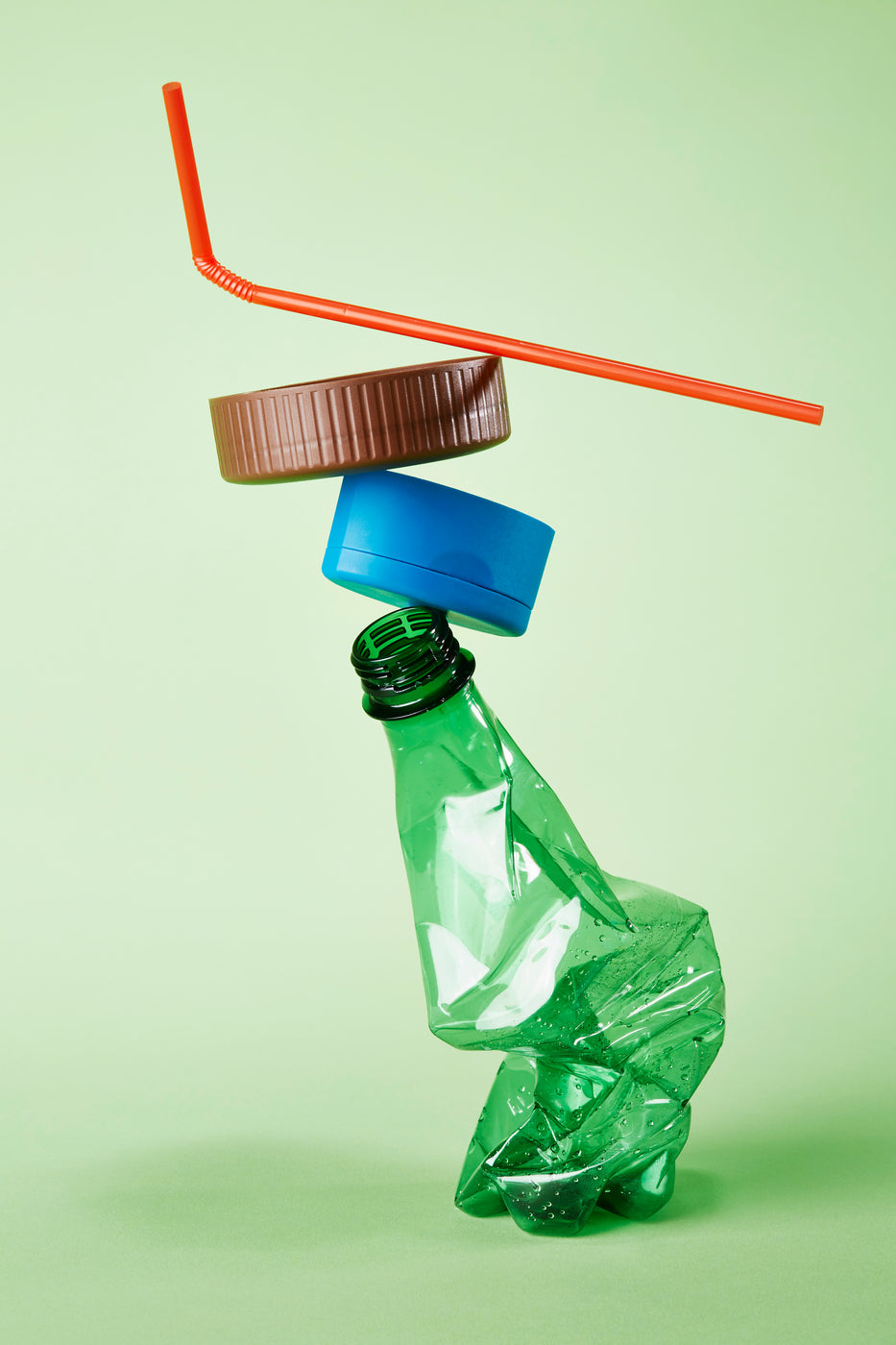 Bottiglia di plastica vuota, tappo e cannuccia impilati davanti a sfondo verde