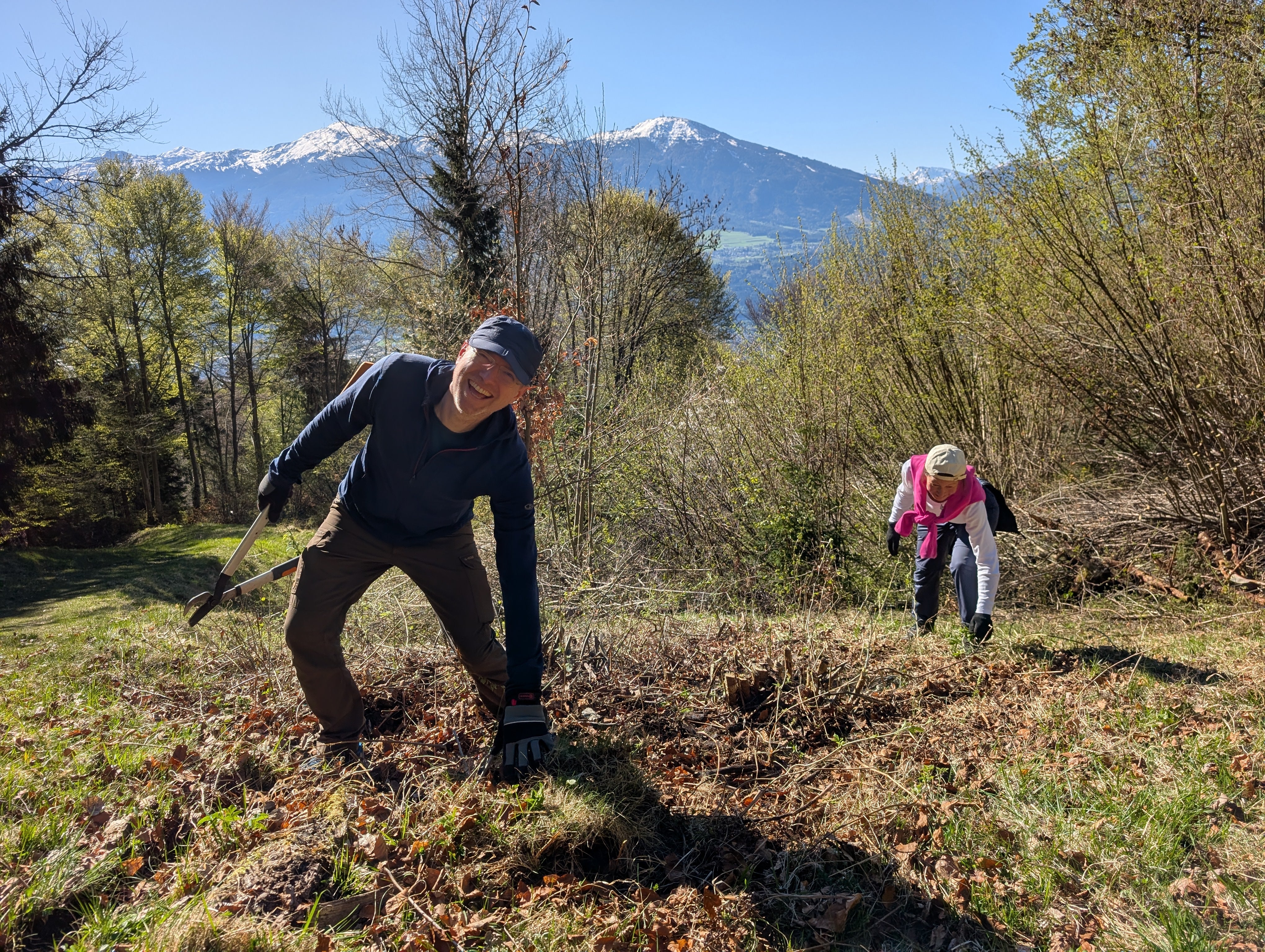 Zwei Personen arbeiten auf einer Wiese vor Bergpanorama 