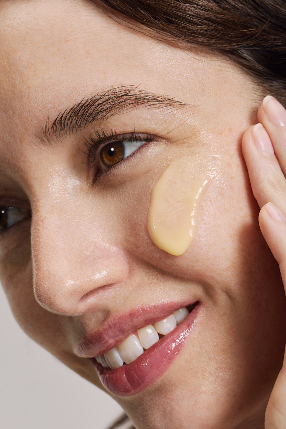 Primo piano di una donna sorridente con crema dorata sotto l'occhio