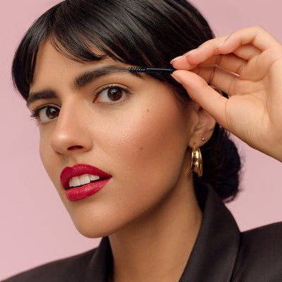 Donna spazzola il sopracciglio con uno spazzolino su sfondo rosa