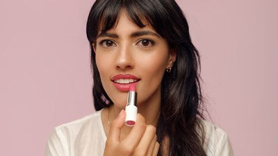 Donna applica rossetto rosa davanti a sfondo rosa