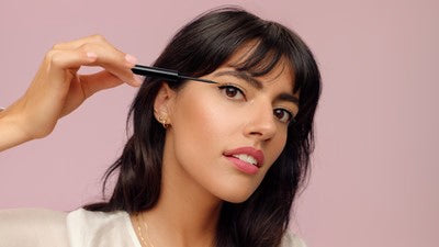 Donna applica eyeliner su sfondo rosa