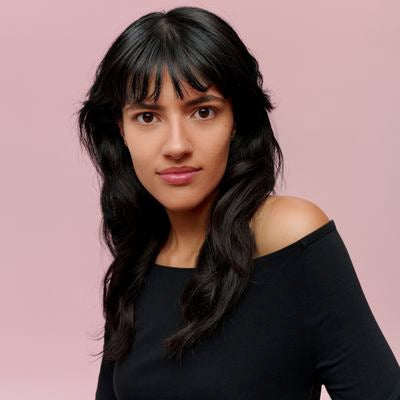 Ritratto di una donna con capelli neri e frangia su sfondo rosa