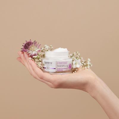 Mano tiene un barattolo aperto di crema giorno rassodante lavera con fiori