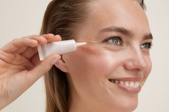 Donna sorridente applica un Hydrating Fluid sulla guancia