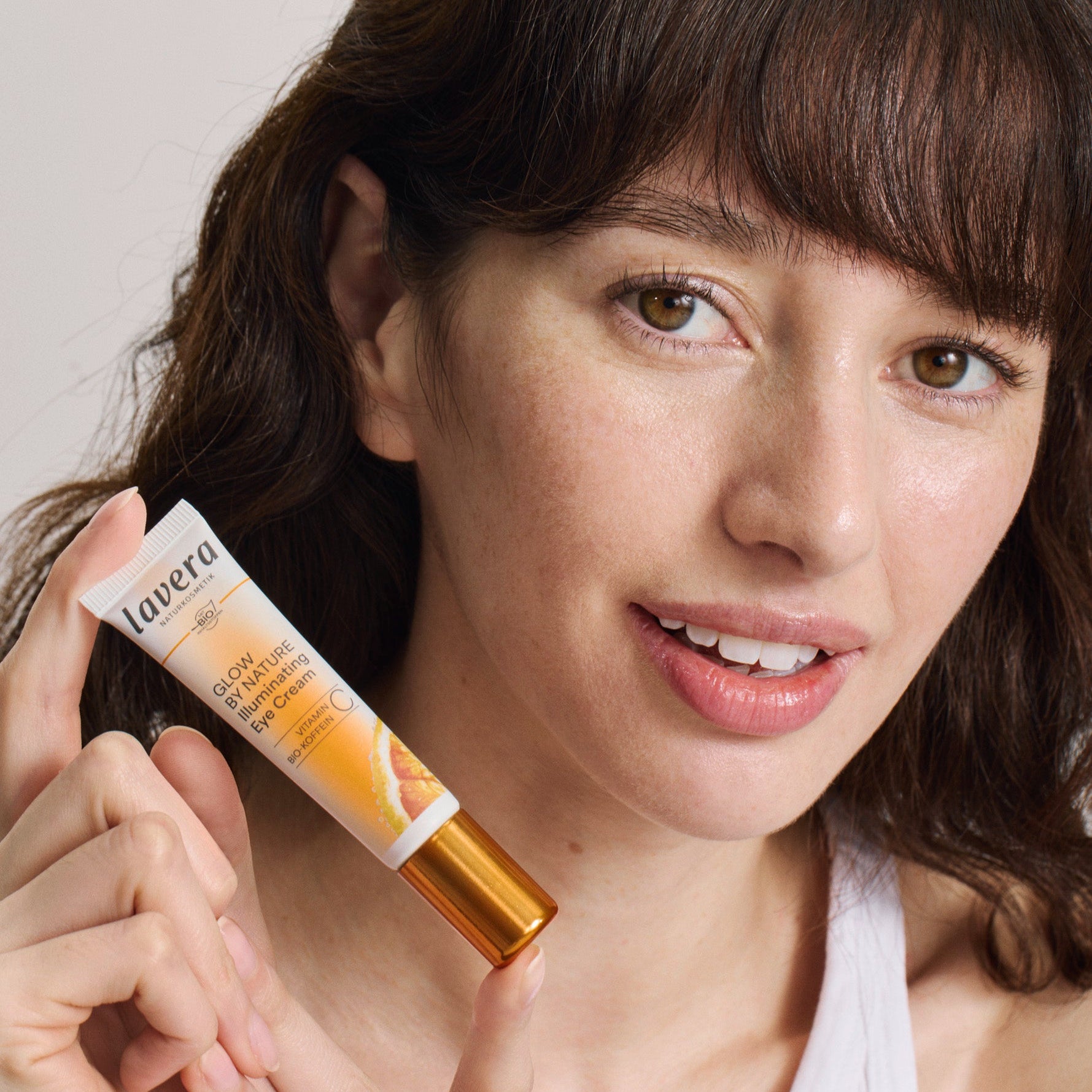 Eine Frau hält die lavera Glow by Nature Illuminating Eye Cream in der Hand