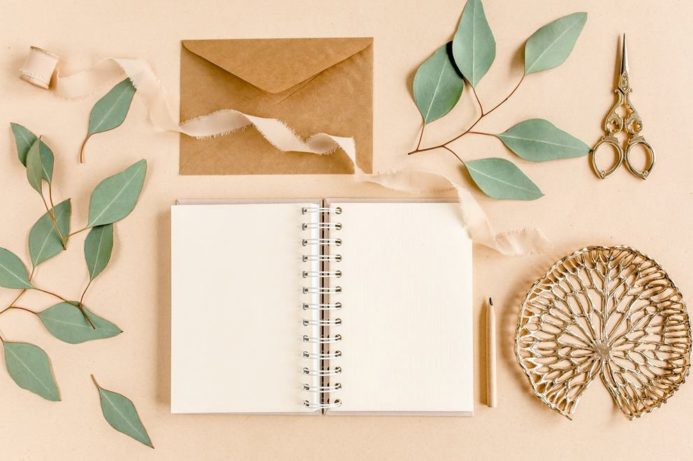 Quaderno bianco con busta, foglie di eucalipto, forbici e decorazioni in flatlay