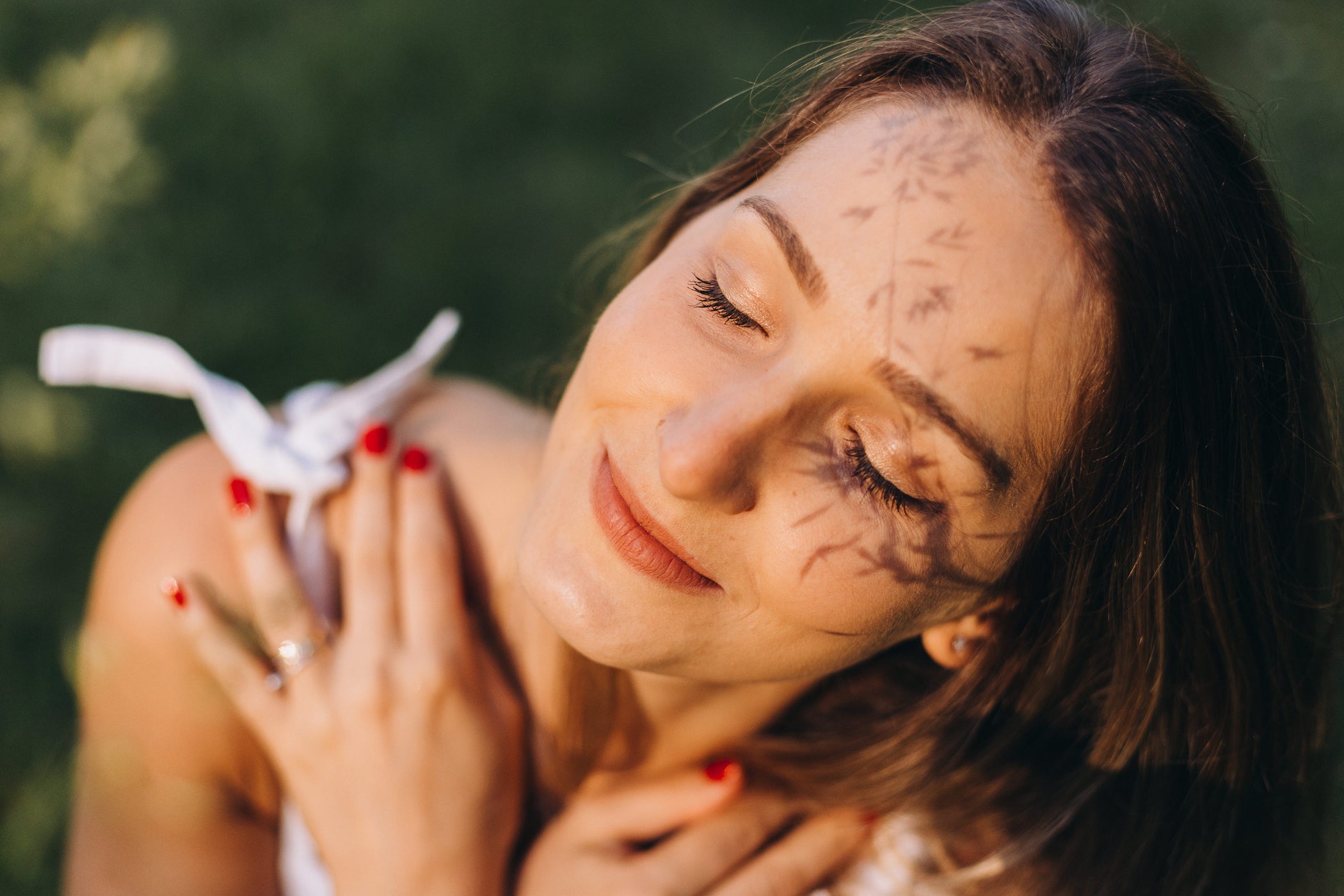 Primo piano del viso di una giovane donna con occhi chiusi e braccia incrociate sul petto – con luce solare ed effetti d'ombra