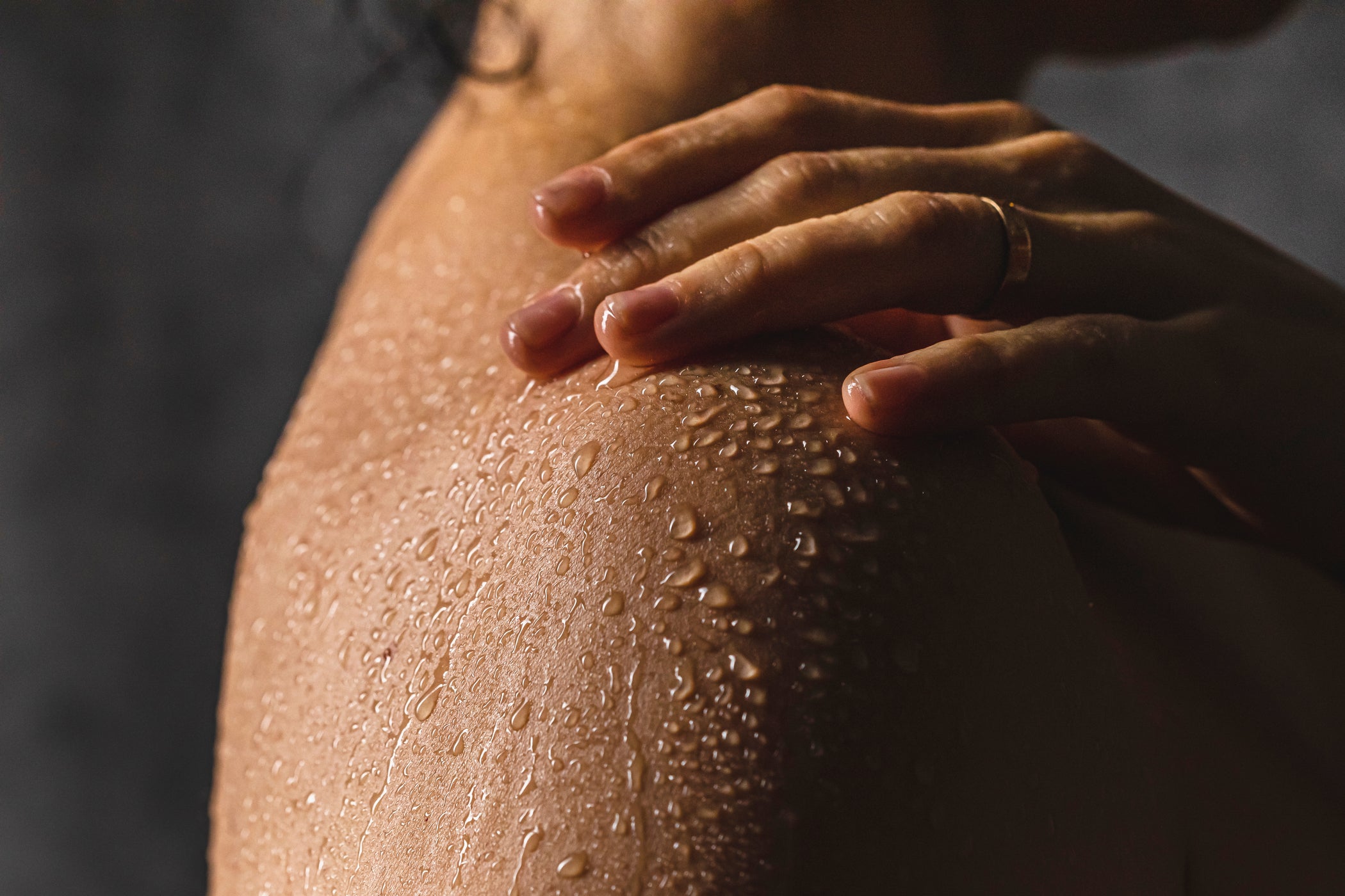 Primo piano della zona spalle di una persona femminile coperta di gocce d'acqua su sfondo scuro