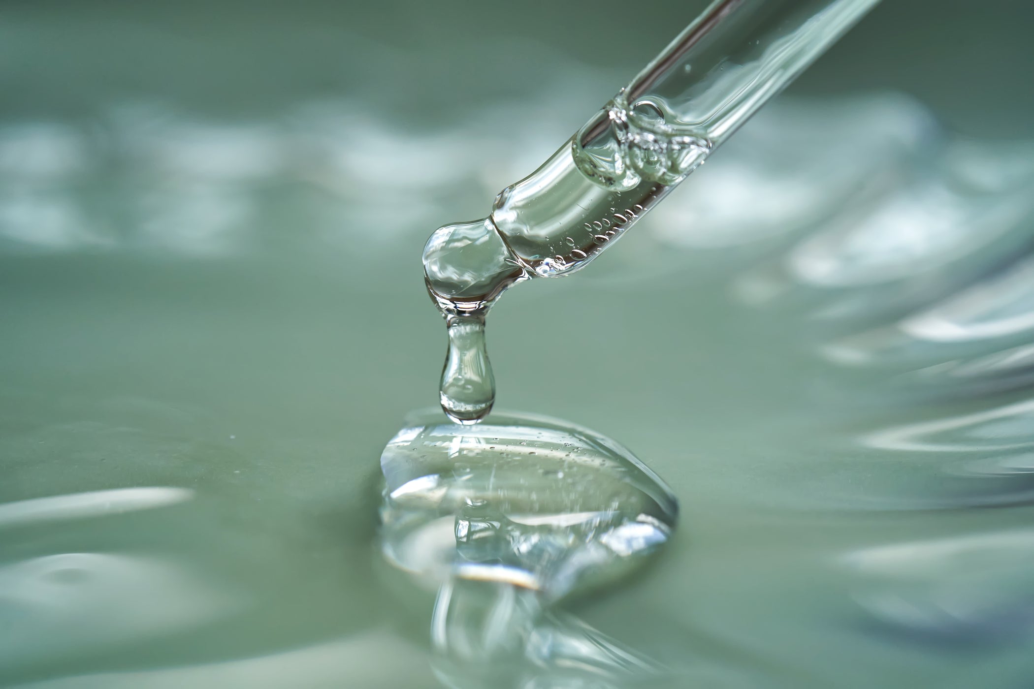 Pipetta che lascia cadere siero trasparente su superficie gel lucida, ripresa macro