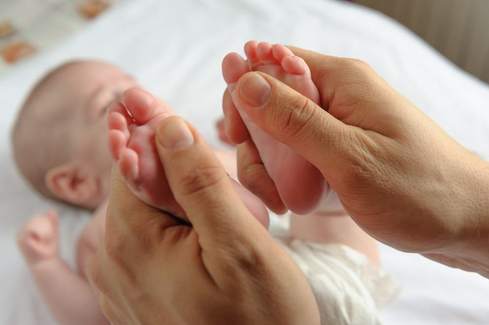 Un neonato è sdraiato sulla schiena su una coperta e viene massaggiato su entrambi i piedi.