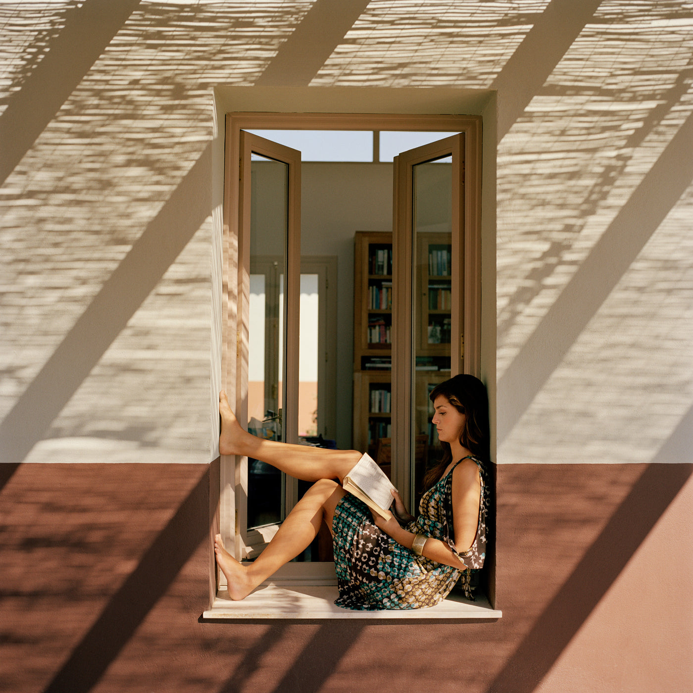 Donna con lunghi capelli scuri seduta a leggere in una finestra con luce naturale e ombre
