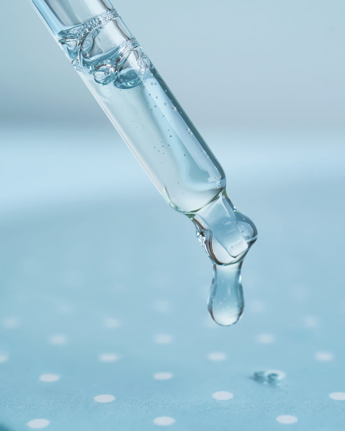 Pipette lässt klaren Serum-Tropfen fallen, Makro auf blauem Hintergrund