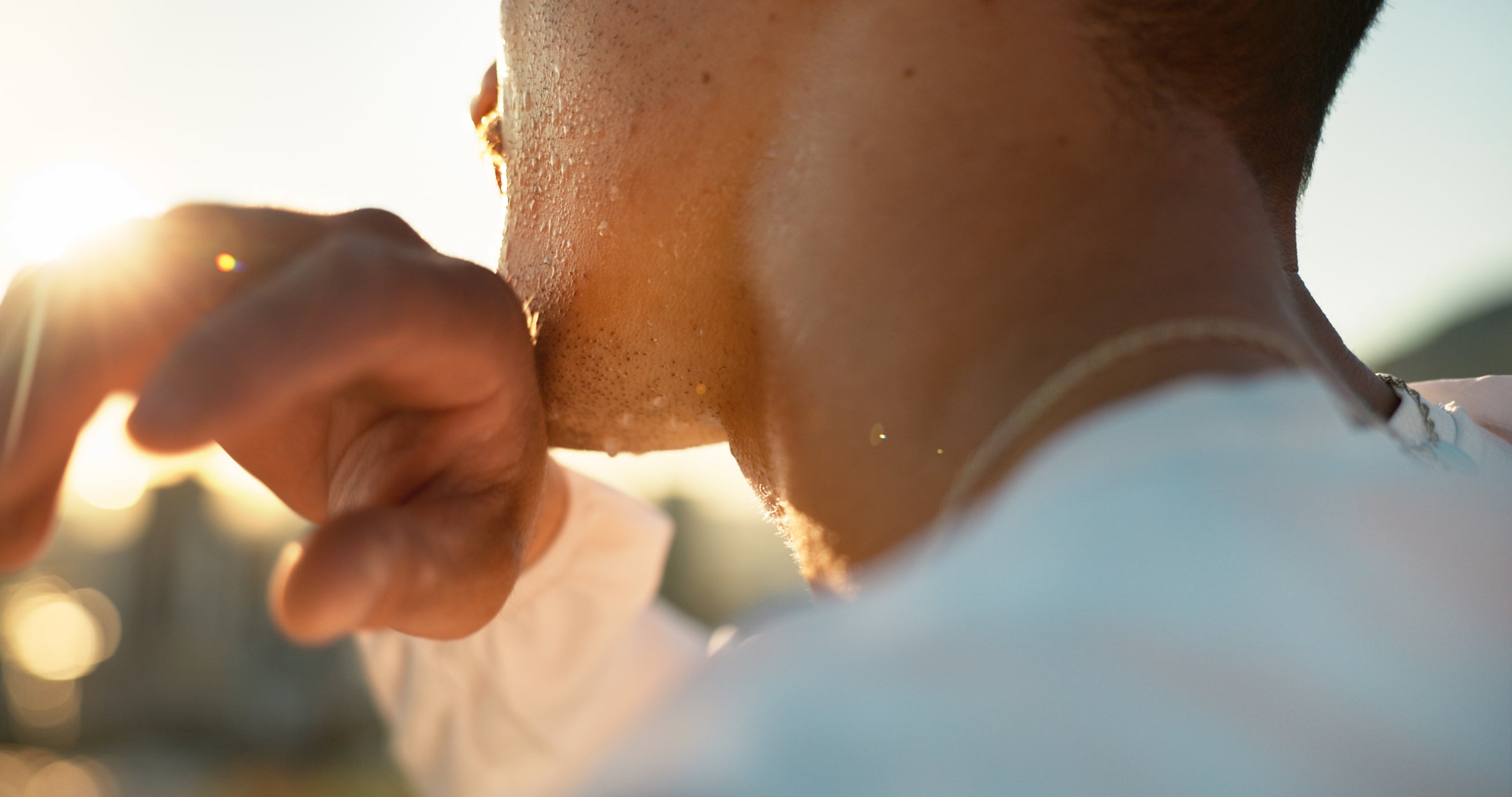 Uomo asciuga il sudore dal viso con un asciugamano, luce del sole sullo sfondo