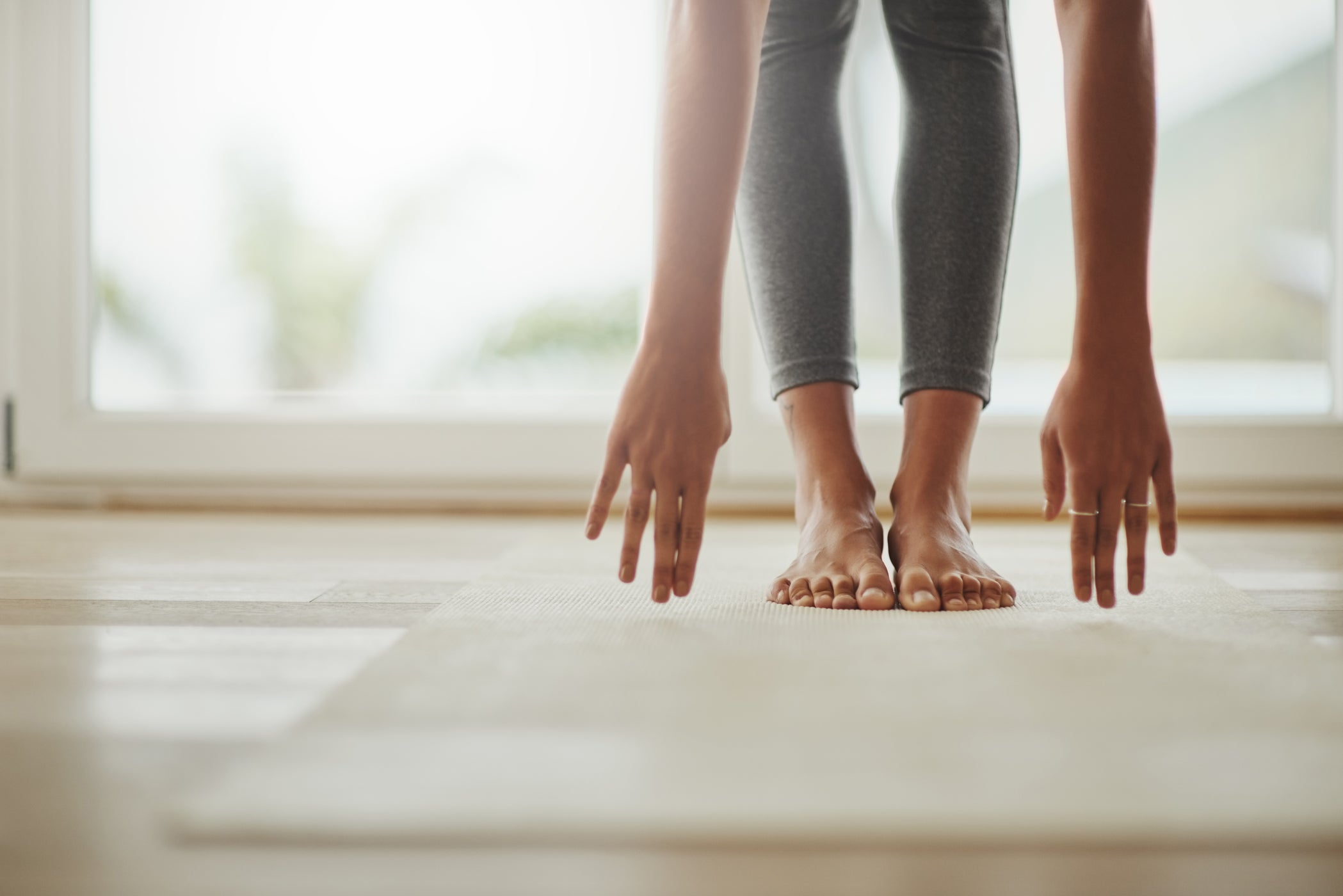 Parte inferiore delle gambe e delle braccia di una donna in piedi su un tappetino da yoga