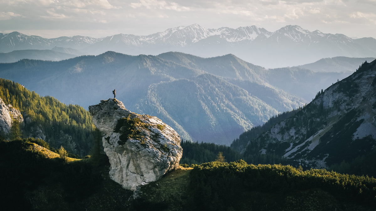 Persona in piedi su una grande roccia in un paesaggio montano verde
