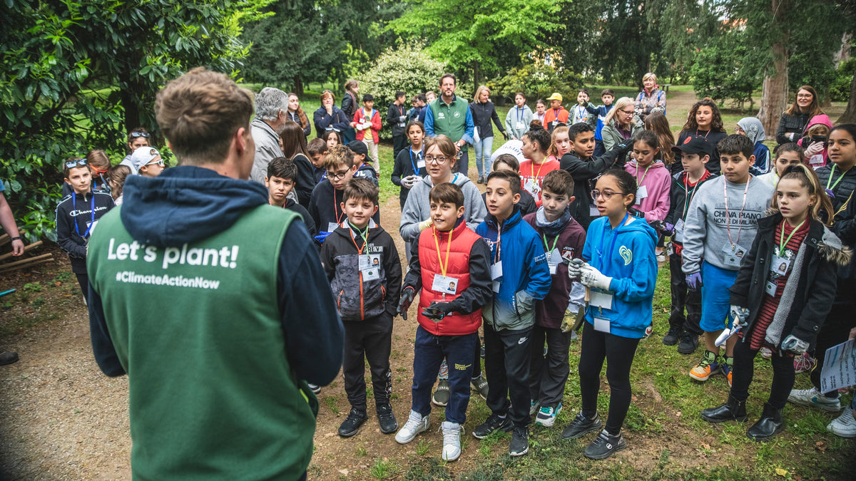 Giovane uomo con gilet verde racconta davanti a un gruppo di bambini all'aperto nel verde