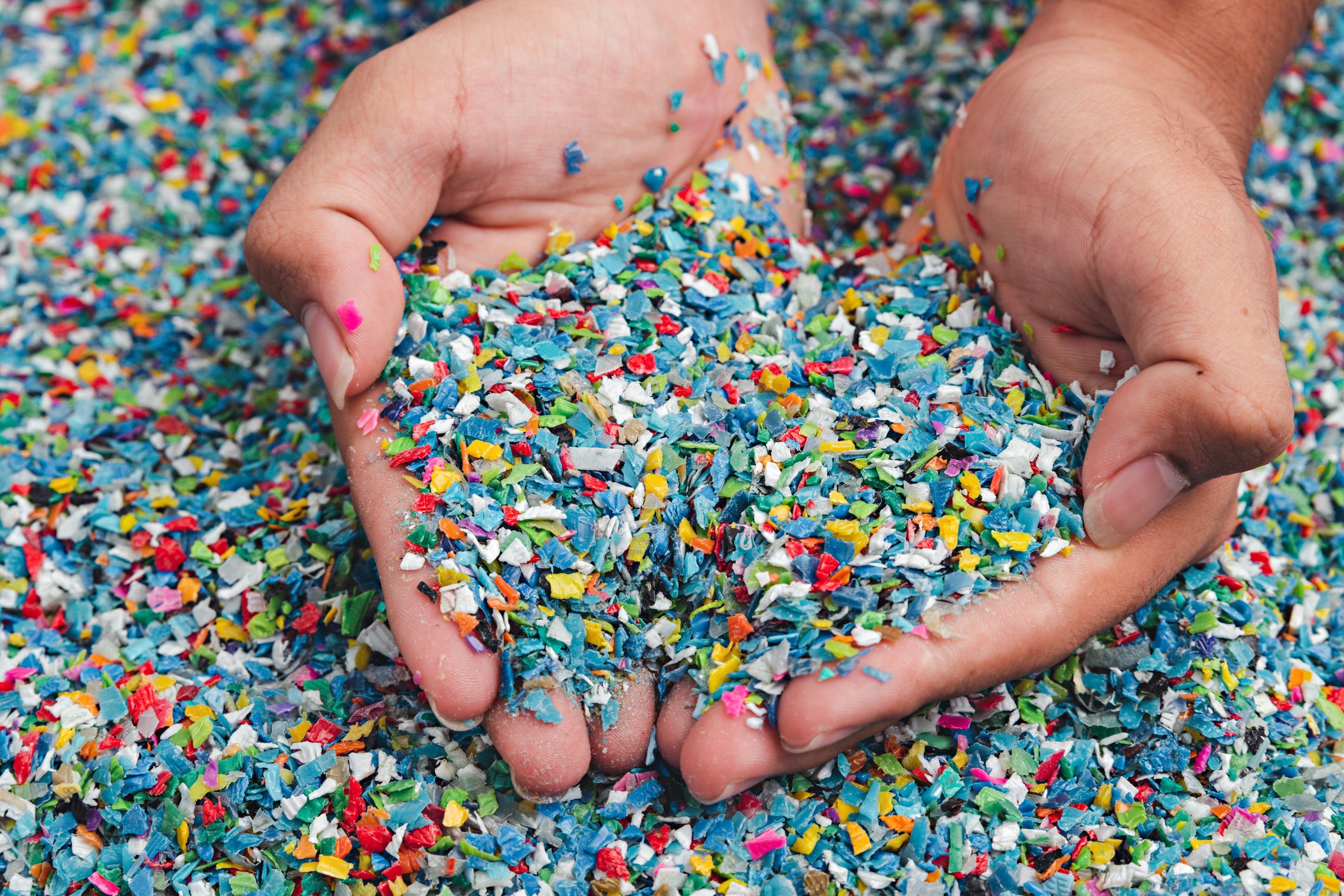 Zwei Hände halten buntes Plastikgranulat, das recycelt wird