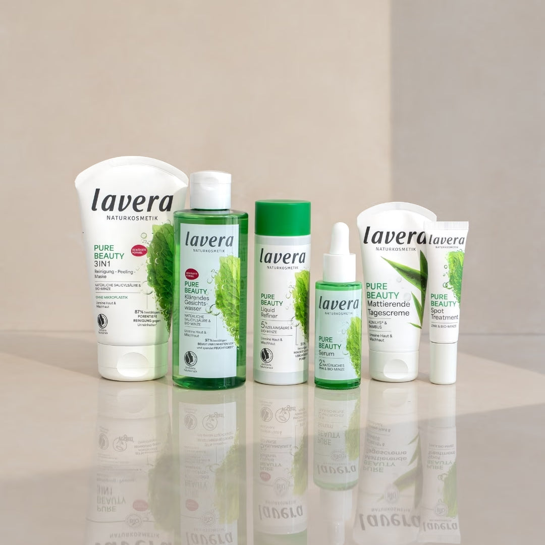 I prodotti per la cura del viso lavera Pure Beauty sono disposti su una superficie riflettente davanti a uno sfondo chiaro diviso in due parti.