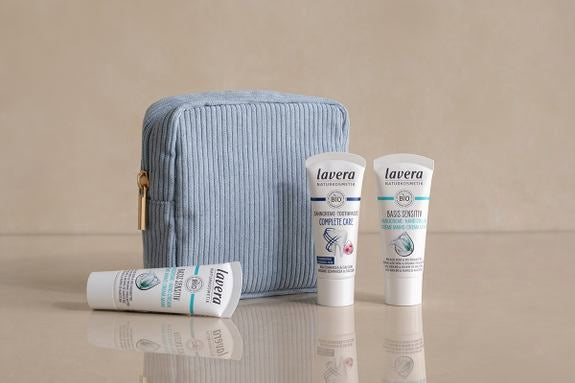 Blaue Kosmetiktasche mit drei lavera Reisegrößen auf beigem Untergrund