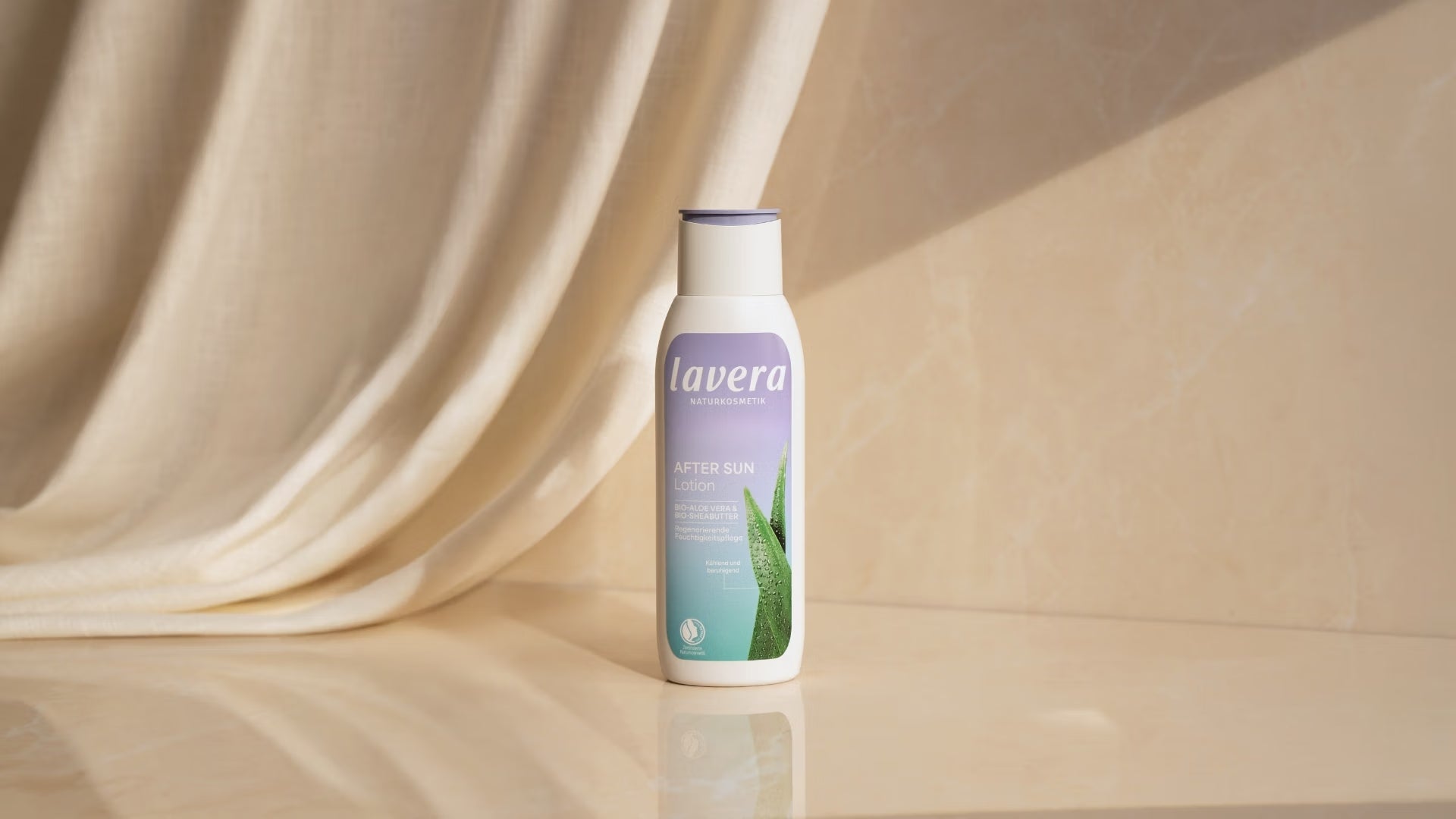 lavera After-Sun-Lotion steht vor hellem Stoff auf einer spiegelnden Oberfläche im warmen Sonnenlicht.