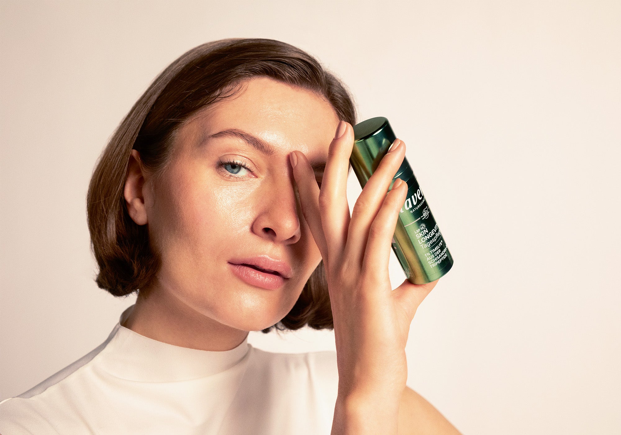 Donna con capelli castano scuro alle spalle tiene in mano Skin Longevity trattamento giorno