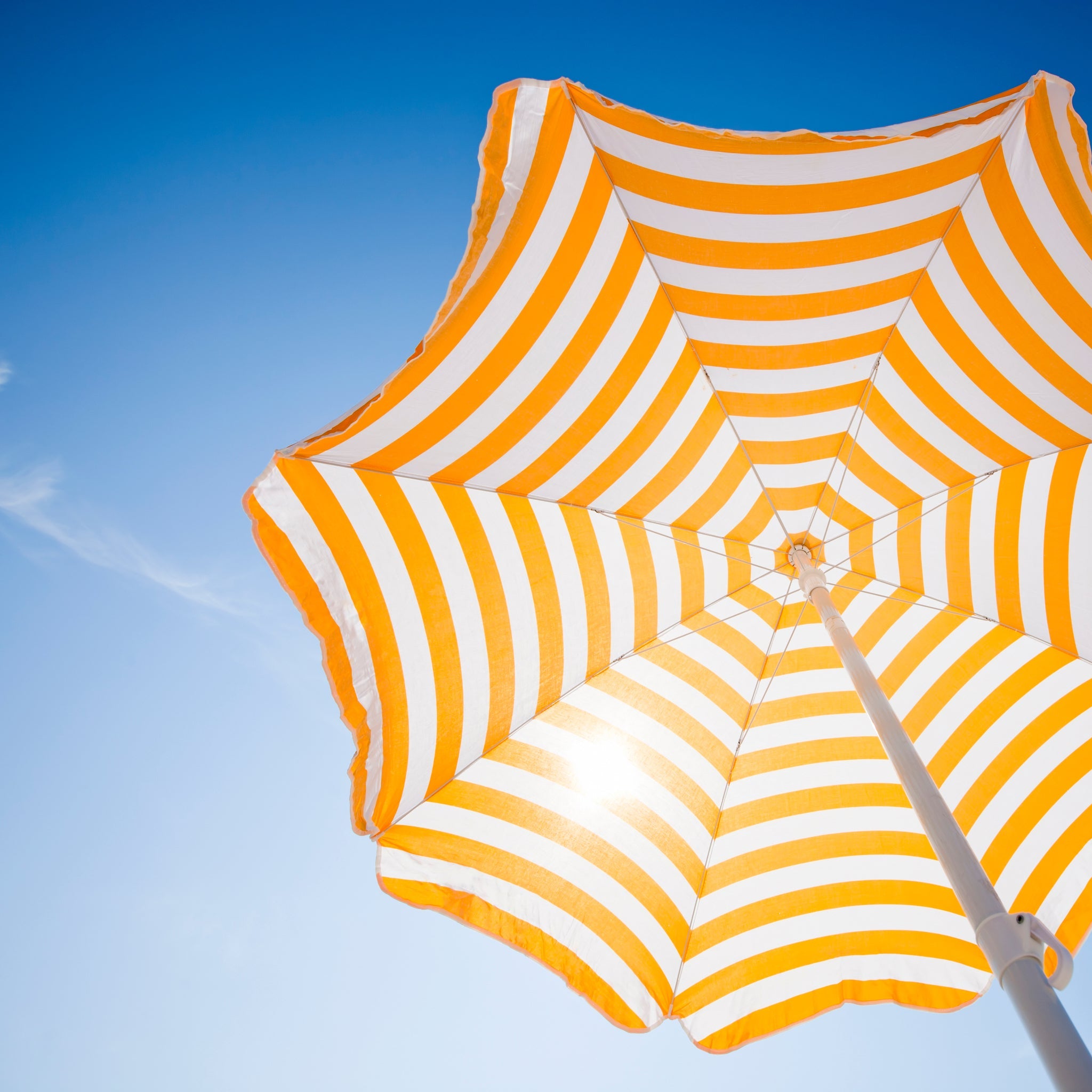 Gelb-weiß gestreifter Sonnenschirm von unten fotografiert vor blauem Himmel.