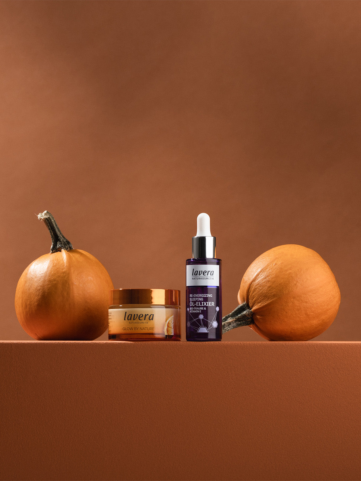 Glow by Nature Creme und Re-Energizing Öl-Elixier zwischen 2 Kürbissen