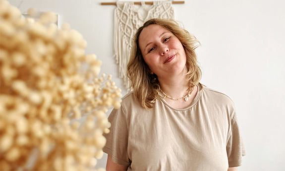 Donna sorride leggermente con la testa inclinata davanti a decorazione macramè