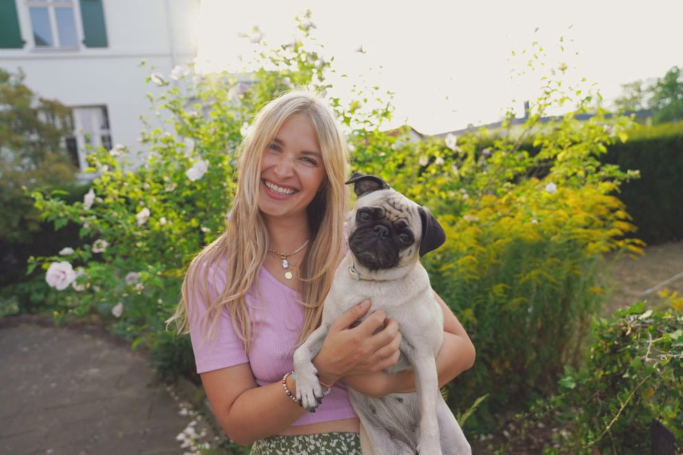 Blonde Frau lächelt und hält Mops im Arm
