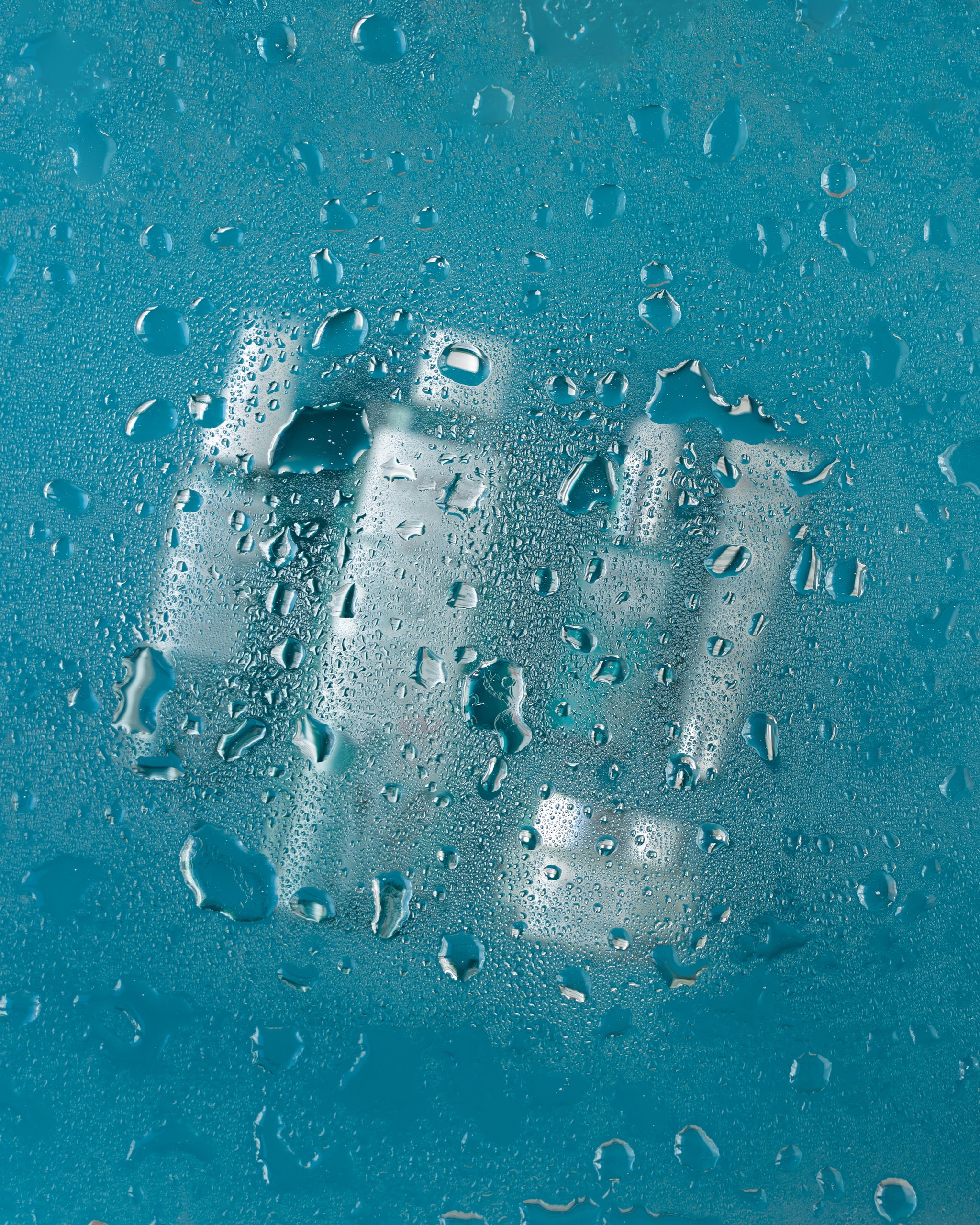 Wassertropfen auf Glas, dahinter unscharfe Pflegeprodukte in blauer Szenerie