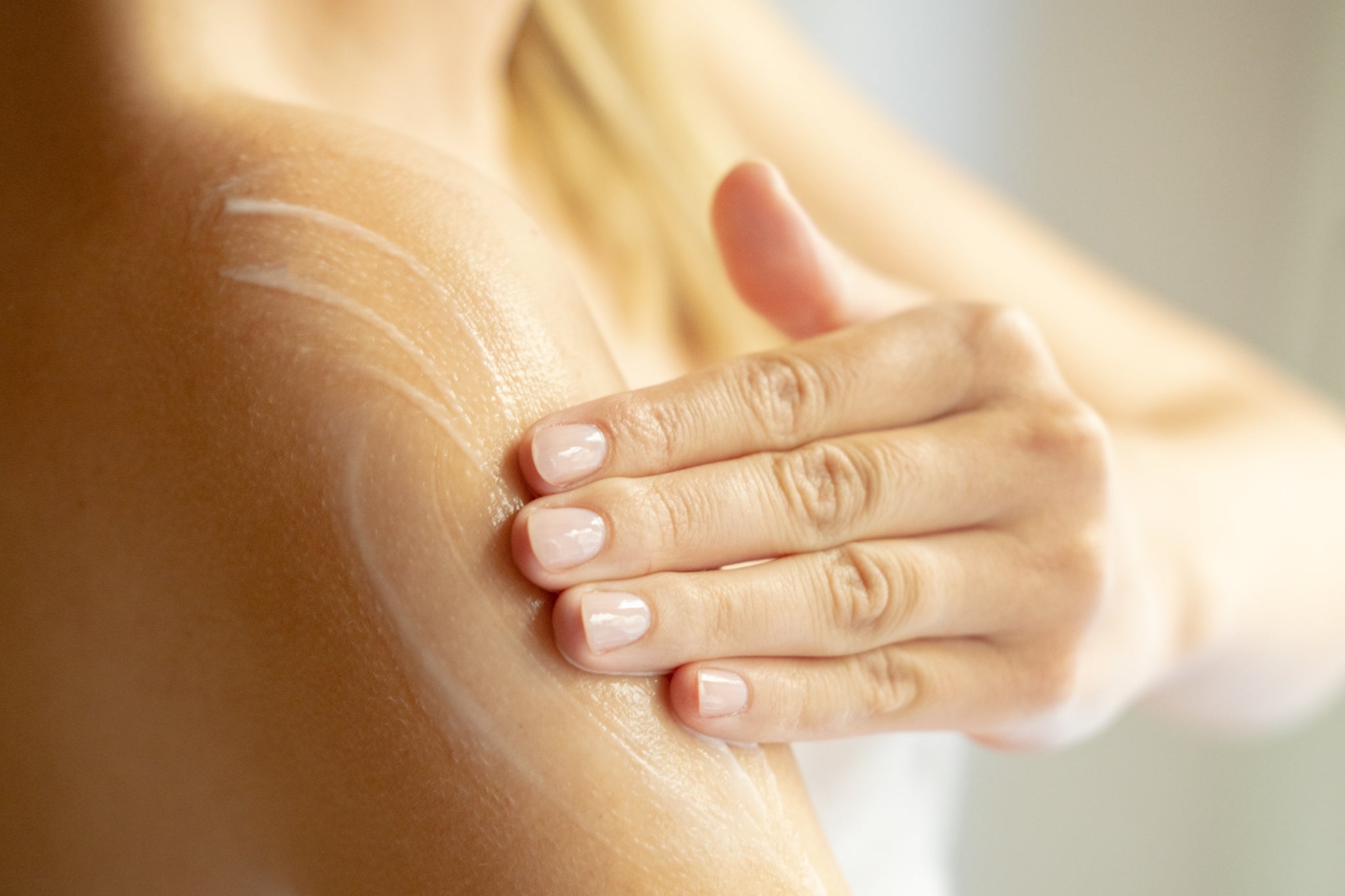 Hand trägt Creme auf nackte Schulter auf, Nahaufnahme.