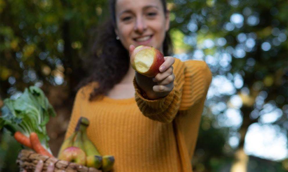 Donna tiene mela morsicata e cesto con frutta e verdura