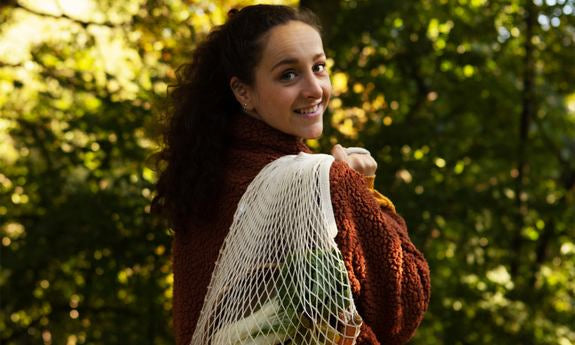 Donna con borsa della spesa a rete sulla spalla guarda indietro sorridendo