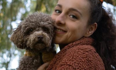 Donna tiene piccolo cane in braccio e sorride verso la camera