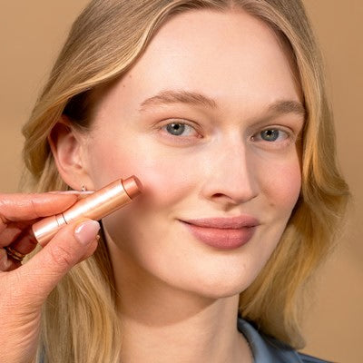 Giovane donna con capelli biondi che sorride alla telecamera applicando colore sulla guancia