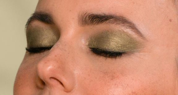 Primo piano della metà centrale del viso di una donna con trucco occhi verde scuro in vista laterale e occhi chiusi