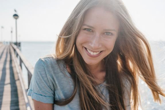 Lächelnde Frau mit langen Haaren auf einem Steg am Meer
