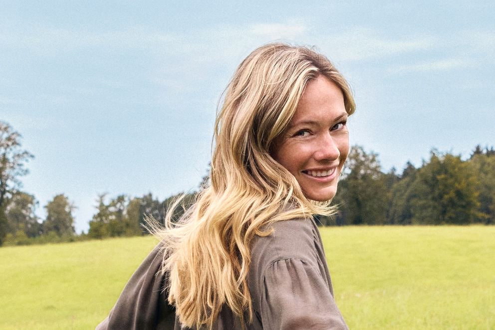 Donna bionda sorride sopra la spalla su prato verde, ritratto outdoor