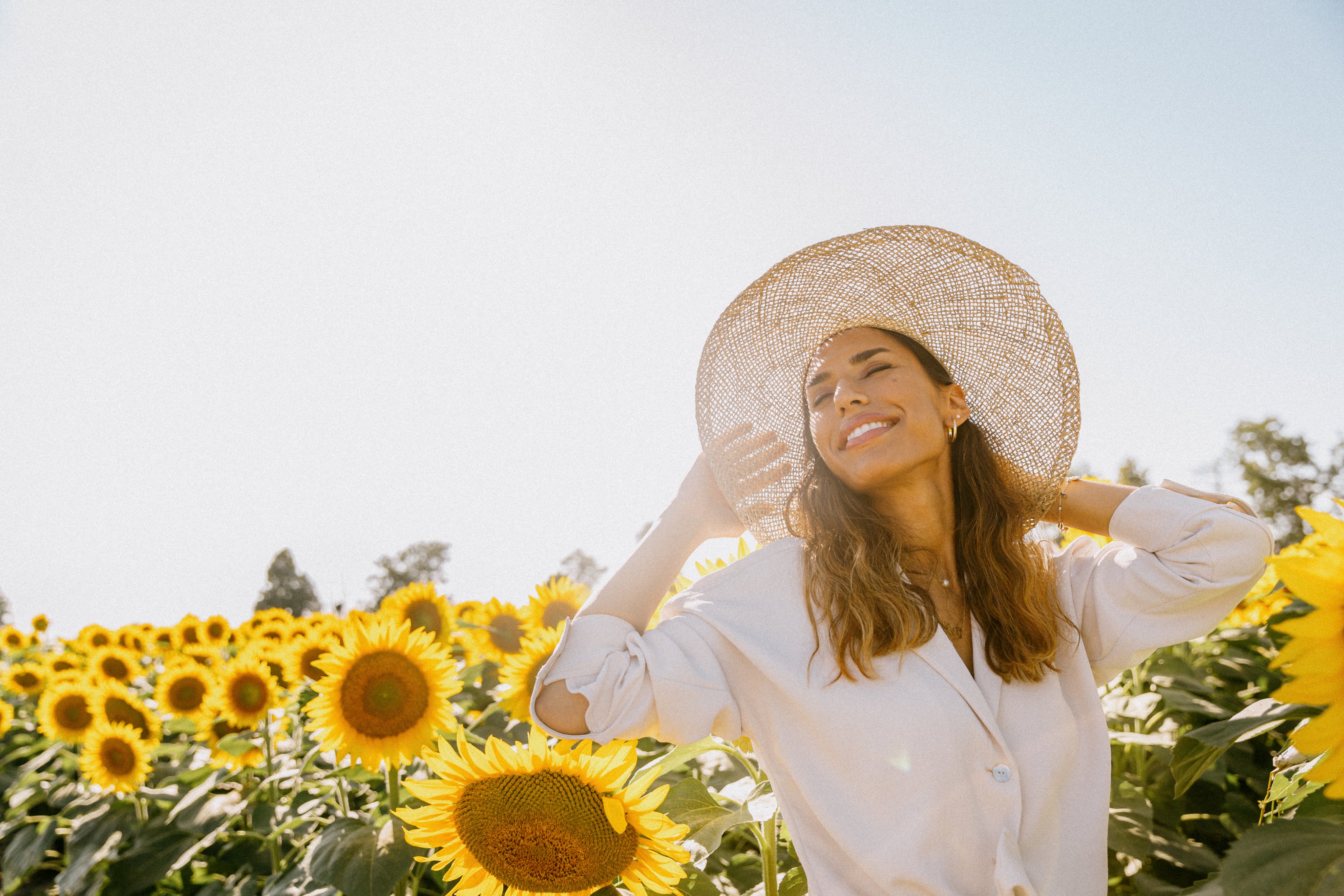 Frau mit Strohhut im Sonnenblumenfeld, blickt in die Sonne, Sommerstimmung